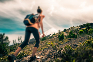 Young woman hiker walks on the loose rocky trail with snow capped volcano on the background....
