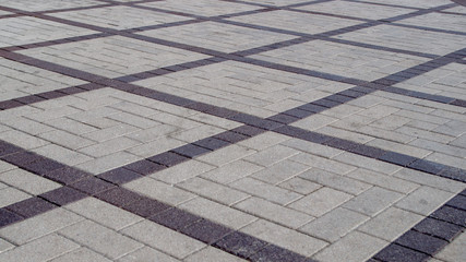Street square area lined with rectangular gray paving slabs with drawings in the form of a rhombus of brown tiles. Stone patterned background going into perspective