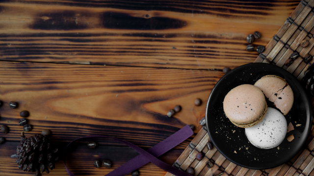 Top view of black plate of coffee macarons on bamboo maton rustic table