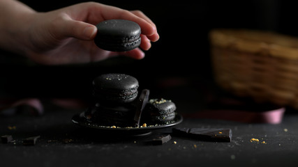 Close up view of a girl picking dark chocolate macaron from black plate