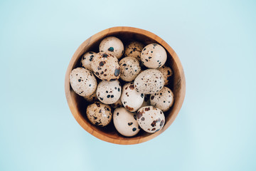 Quail eggs in wooden bowl on a blue background. Easter concept, flay lay photo. Mockup, space for text.