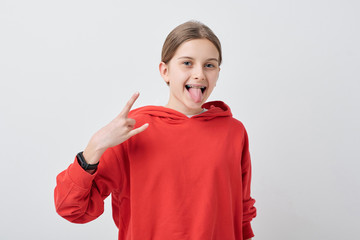 Portrait of crazy cool teenage girl in braces showing horn gesture and sticking tongue out against...