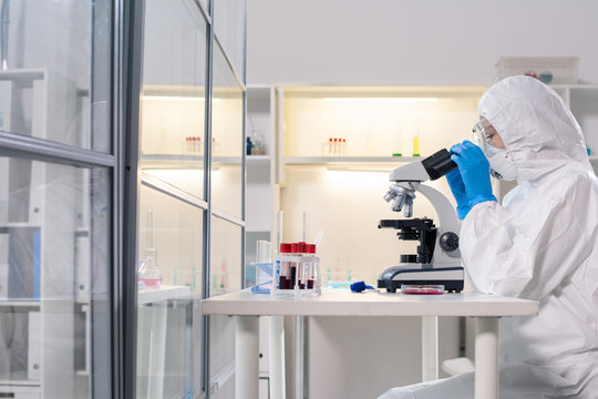 Side view of medical scientist in protective mask using microscope while studying dangerous coronavirus in laboratory - Powered by Adobe
