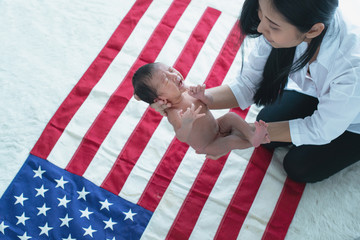 Asian mother holding newborn baby over American flag, newborn baby crying, celebrating 4th July independence day