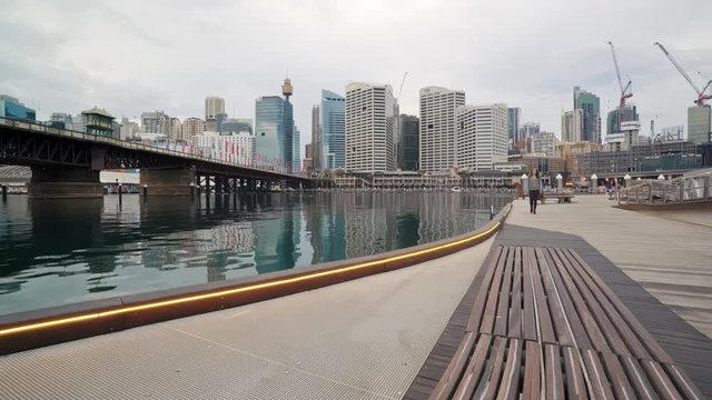 Still shot of Darling Habour, Sydney on an overcast day as an attractive woman walks past admiring the cityscape. 