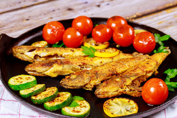 Fried small fish with tomato and lemon in a pan on a wooden background.