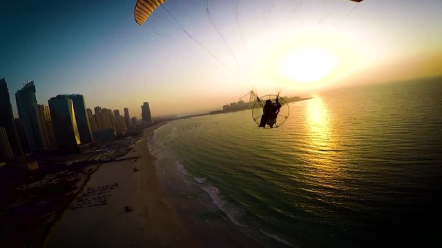 Paramotoring powered paragliding ppg flight high in beautiful evening sunset sky on calm blue Dubai beach ocean seascape