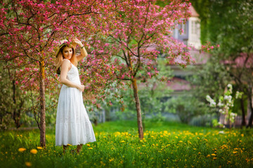 portrait of a beautiful girl in a hat and white dress in a blooming garden