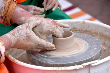 A human Potter works on a Potter's wheel, making a ceramic pot from clay in a pottery workshop.