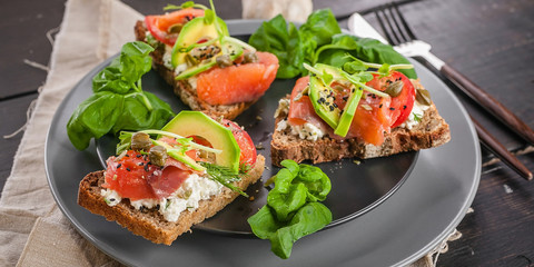 Food banner. Delicious bruschettas with smoked salmon, curd cheese, avocado, basil and chia seeds. Tasty and healthy breakfast or snack. Mediterranean Kitchen. Close up. Horizontal shot