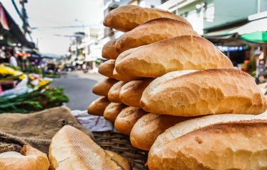 Freshly baked loaves of bread, laid out in a stack for sale on the street market. Closeup view of the bread. In the background is a city street.