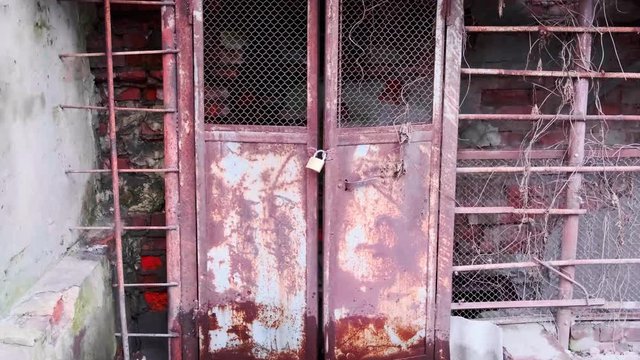 Entrance to an old abandoned ruined building, iron old rusty doors closed with a padlock