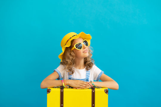 Portrait of happy child with yellow suitcase against blue background