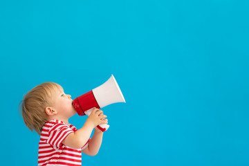 Happy child shouting by megaphone against blue background