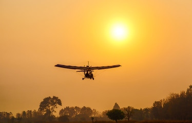 Fototapeta na wymiar Ultralight trike flying with a pilot and a passenger against sunset sky, A microlight aircraft with two passengers with the sun
