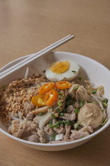 Rice noodles tom yum with pork,fish ball in white bowl on the table; spicy thai noodled.