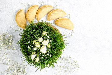 Fototapeta na wymiar Novruz Azerbaijan traditional table setting, delicious sweet pastry on light background with green wheat grass semeni. Golden plate of pakhlava and shekerbura and gogal, copy space