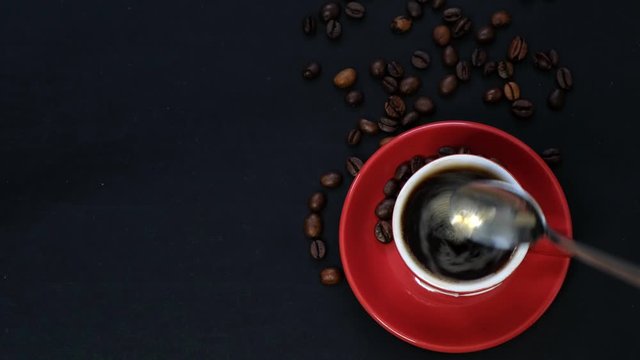 Dark coffee in red cup and coffee beans on black table with copy space. Top view