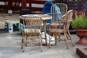 Bamboo garden furniture in shape of small table and three outdoor chairs surrounded with flowers in flower pot and children toys in suburban family house backyard