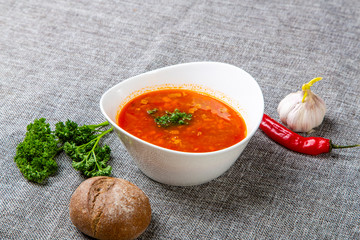 Beef goulash soup with tongue. A white oval plate with red soup stands on a gray canvas. Next to it...