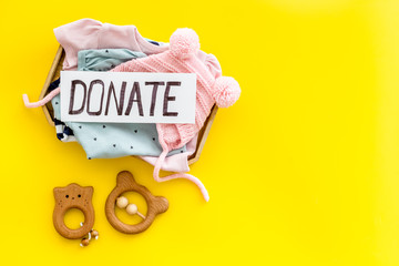 Donate text. Box with clothes for kids on yellow background top-down copy space