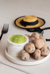Typical Canary Islands dish, Mojo verde or Green sauce with with Papas Arrugadas or wrinkly potatoes and typical canarian hat on wooden table in local restaurant.