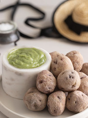 Typical Canary Islands dish, Mojo verde or Green sauce with with Papas Arrugadas or wrinkly potatoes and typical canarian hat on wooden table in local restaurant.