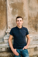Obraz premium Handsome young man on brown background looking at camera. Portrait of laughing young man with hands in pockets leaning against wall. Happy guy smiling.