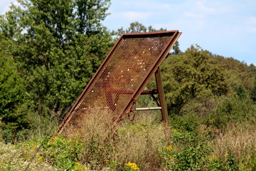 Old vintage retro completely rusted gravel sand sieve screen mesh held together with strong metal frame left at abandoned construction site surrounded with overgrown grass and forest vegetation on cle