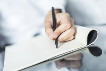 Man writes with a pen in notebook in a sunny office, business and education concept. Close up