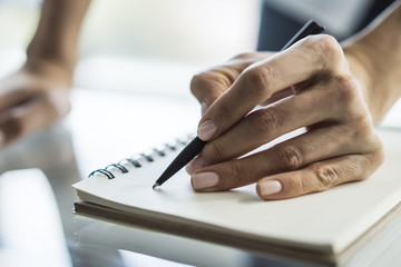 Woman writes with a pen in diary in a sunny office, business and education concept. Close up