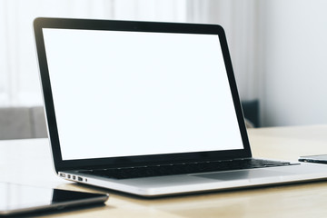 Fototapeta premium Close up of modern laptop with blank screen on wooden table in sunny interior, mockup. Business and technology concept