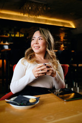 Beautiful Asian woman drinking coffee in warm cosy coffee shop and looking away