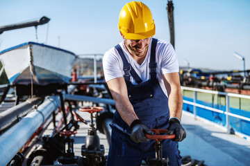 Worthy caucasian smiling workman in overalls and with helmet on head standing on tanker and...