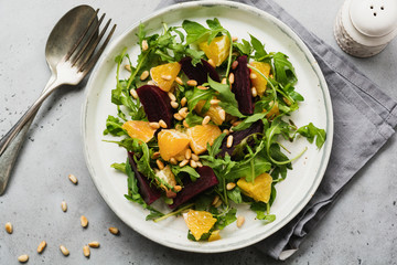 Beets, orange, pine nut, olive oil, feta cheese and arugula salad in ceramic plate on old concrete table background. Top view.