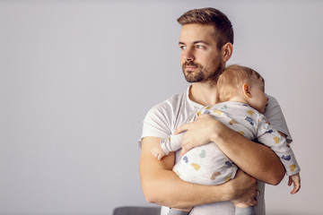 Portrait of handsome father holding his beloved sleeping son and looking away. He is finally...
