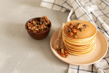 Stack of delicious pancakes with chocolate, honey, nuts and slices of banana on plate and napkin on wooden background