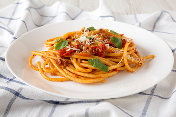 Homemade Bucatini all Amatriciana Pasta in a white plate on cloth, side view. Close-up.