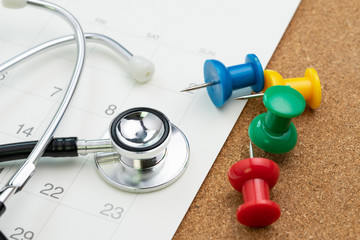 Schedule or appointment for medical exam or meet the doctor for health check up concept, colorful thumbtack or pushpin with white calendar and doctor stethoscope