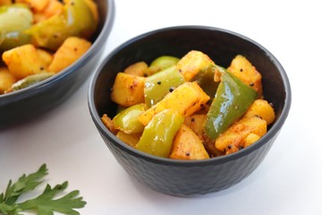 Dry capsicum and potatoes curry. also known as Aloo shimla mirchi Masala. served in black bowl with chilies and coriander over white background with copy space.