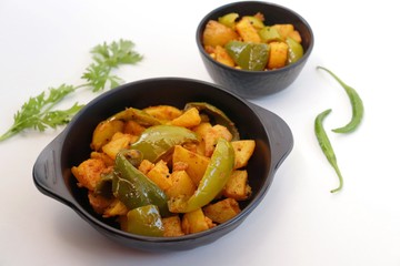 Dry capsicum and potatoes curry. also known as Aloo shimla mirchi Masala. served in black bowl with chilies and coriander over white background with copy space.