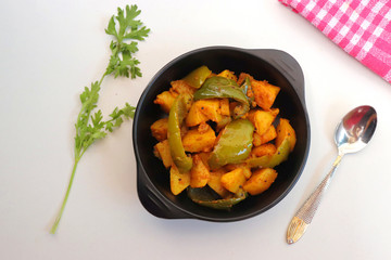 Dry capsicum and potatoes curry. also known as Aloo shimla mirchi Masala. served in black bowl with chilies and coriander over white background with copy space.