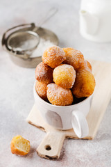 Little Donuts. Home-made cottage cheese cookies deep-fried and sprinkled with icing sugar in a vintage ceramic cup on a light background. Selective focus.