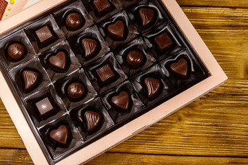 Assorted chocolate candies in a box on wooden table. Top view