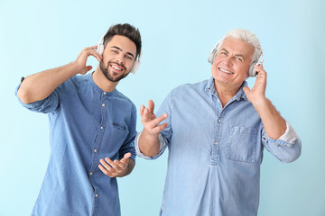 Young man and his father listening to music on color background