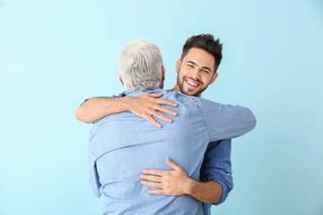 Young man and his father hugging on color background