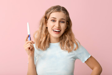 Happy young woman with pregnancy test on color background