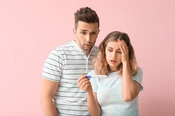 Troubled young couple with pregnancy test on color background