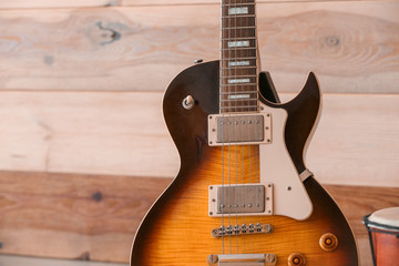 Naklejka premium Electric guitar with sunburst finish and chrome hardware against a rustic wooden wall background
