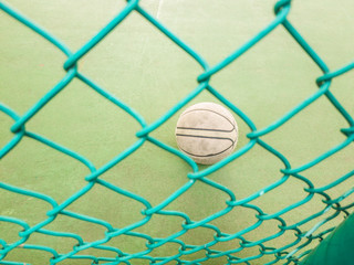 An old, used, dirty basketball behind a wire fence; on a basketball field; inside a school.